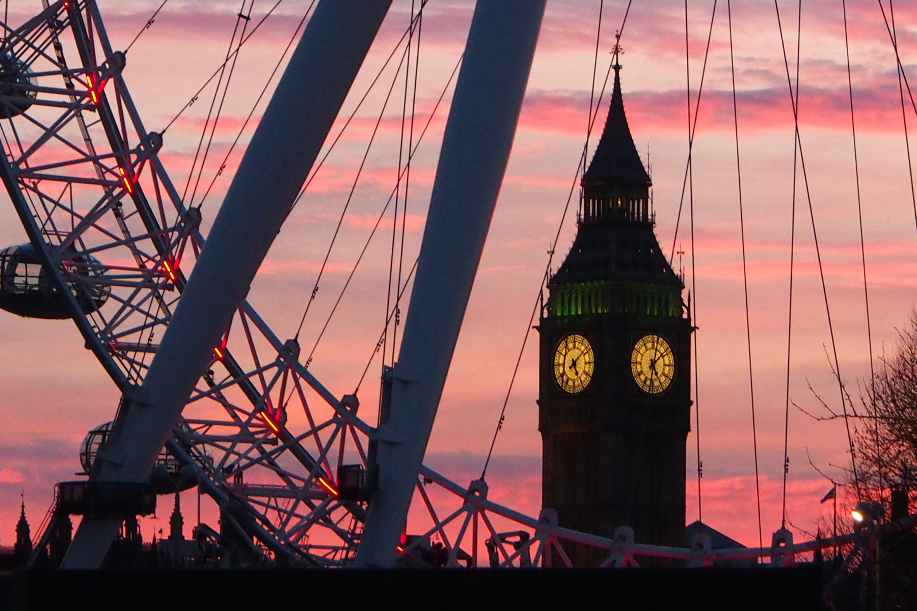A view of Big Ben framed by the London Eye during a pink sunset.