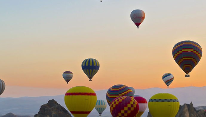 Hot air balloons rise in front of sunrise.