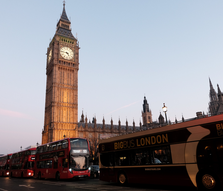 Buses drive past Big Ben at sunset.