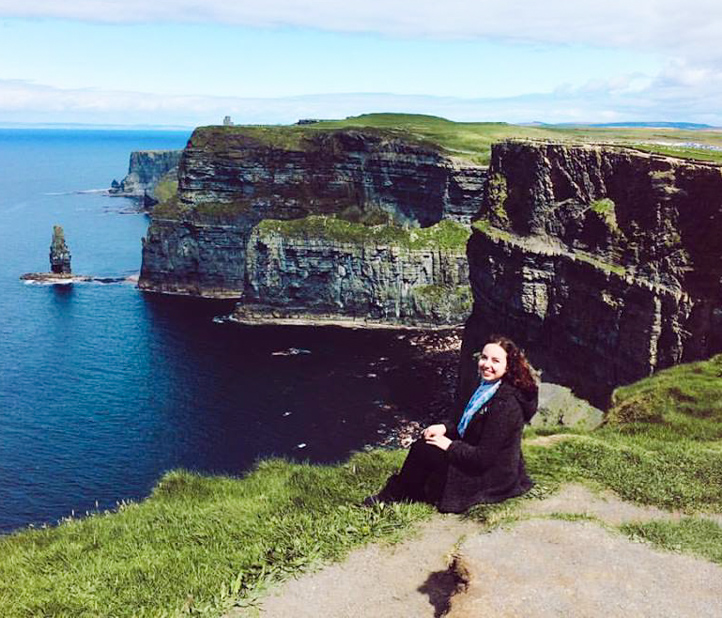 Woman sits beside Cliffs of Moher.