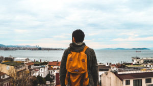 Man wearing orange backpack overlooks coastal town.