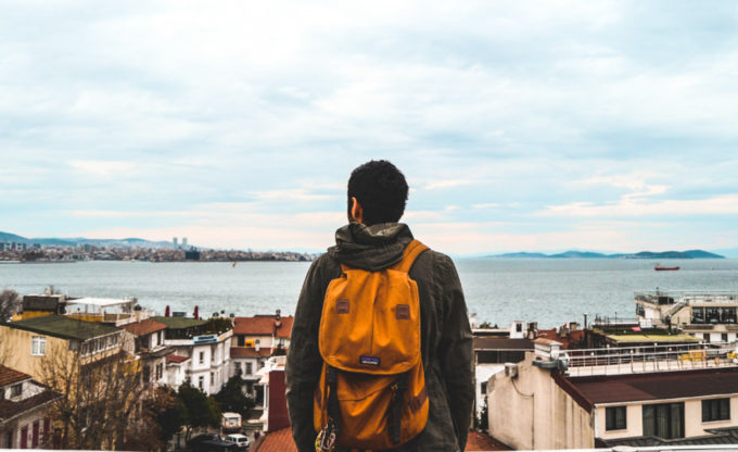 Man wearing orange backpack overlooks coastal town.