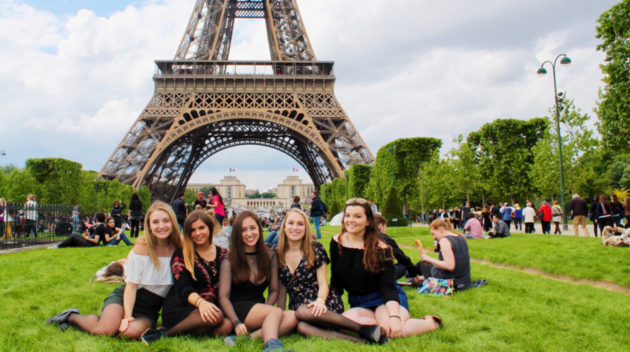 Student group sits on lawn in front of Eiffel Tower.
