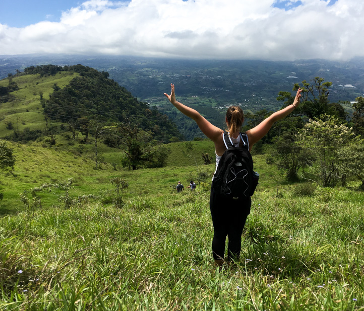 Woman holds arms out while hiking through field.