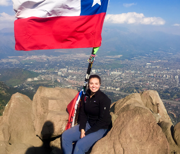 Woman sits on top of mountain with flag.